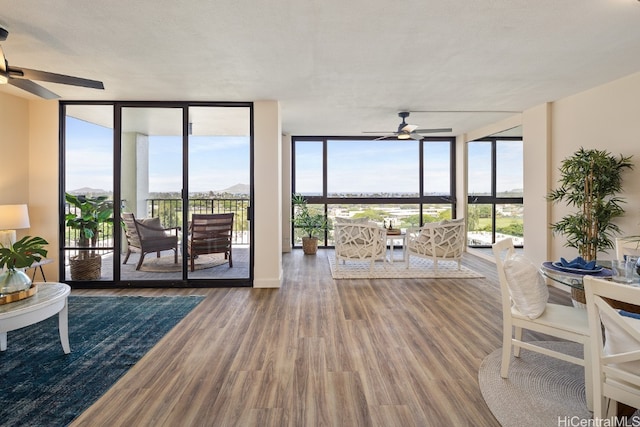 living room with a textured ceiling, a wall of windows, wood-type flooring, and ceiling fan