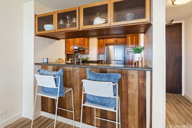 bar featuring dark stone counters, sink, hardwood / wood-style floors, and stainless steel refrigerator