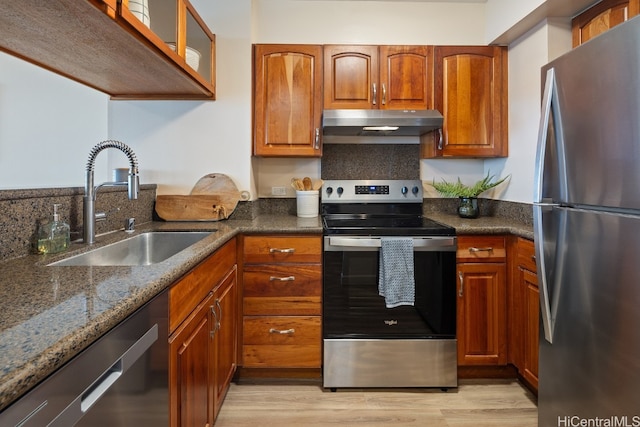 kitchen with dark stone countertops, sink, light wood-type flooring, and appliances with stainless steel finishes