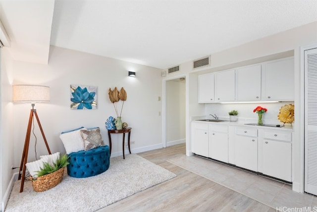 kitchen with light wood-type flooring, white cabinetry, and sink