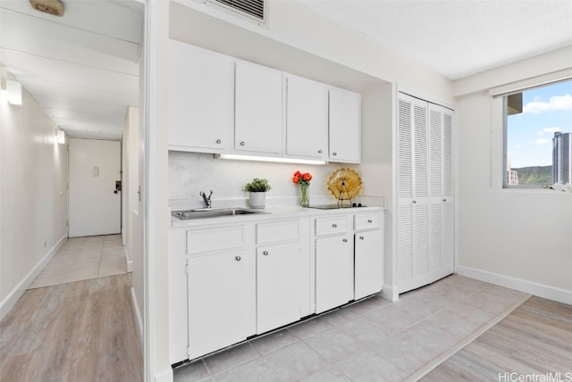 kitchen with white cabinets, light wood-type flooring, sink, and a textured ceiling