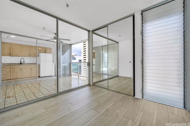 interior space featuring expansive windows, light hardwood / wood-style floors, ceiling fan, and sink