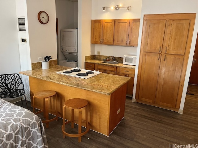 kitchen featuring sink, kitchen peninsula, stacked washer / drying machine, white appliances, and dark wood-type flooring