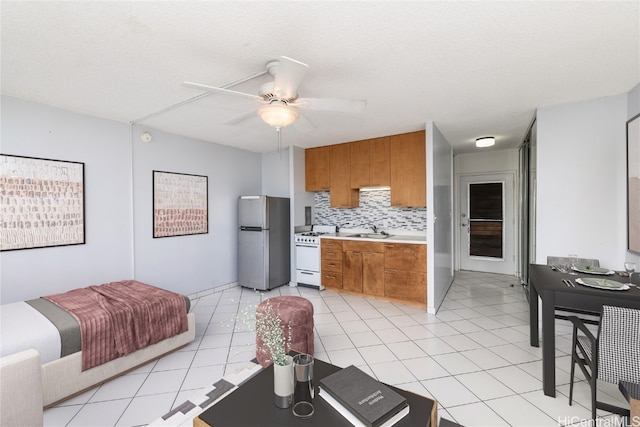 kitchen with stainless steel refrigerator, light tile patterned floors, decorative backsplash, gas range gas stove, and ceiling fan