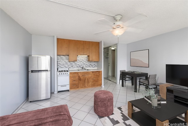 kitchen featuring stainless steel fridge, white gas range, decorative backsplash, sink, and ceiling fan