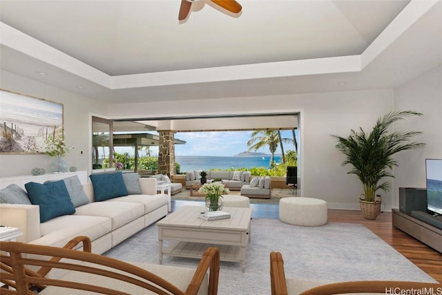 living room with a ceiling fan, a raised ceiling, baseboards, and wood finished floors