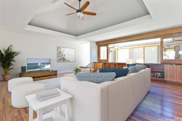 living room with a tray ceiling, wood finished floors, and a ceiling fan