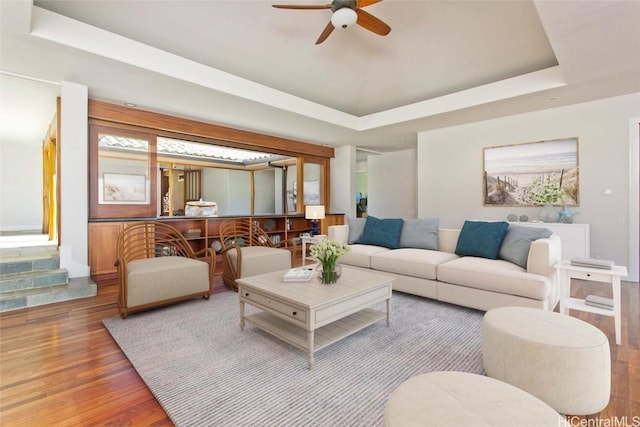 living area featuring ceiling fan, a tray ceiling, and wood finished floors