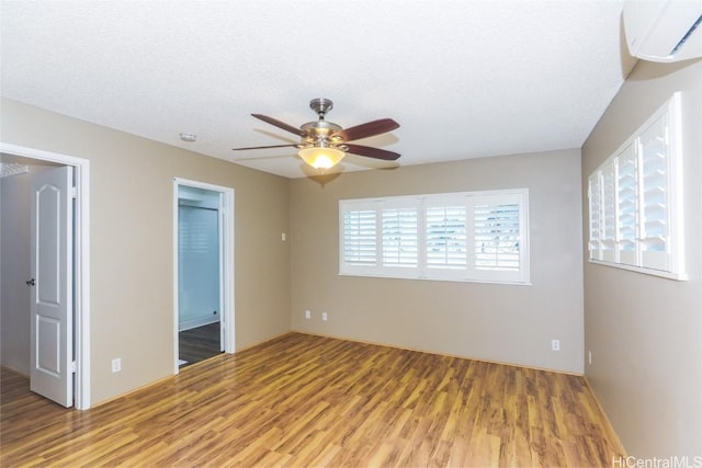 unfurnished bedroom with a wall mounted air conditioner, ensuite bathroom, ceiling fan, a textured ceiling, and wood-type flooring