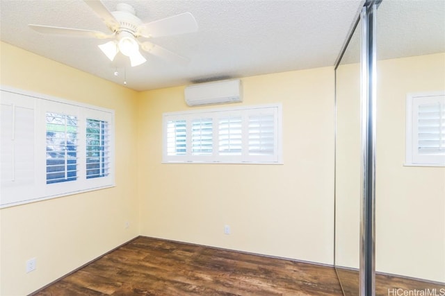 spare room with dark hardwood / wood-style flooring, a textured ceiling, a wall mounted AC, and ceiling fan