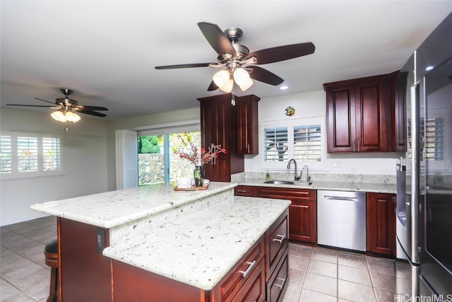 kitchen with light stone countertops, a center island, sink, stainless steel dishwasher, and light tile patterned floors