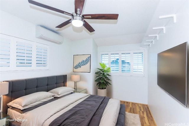 bedroom with a wall mounted air conditioner, light hardwood / wood-style floors, and ceiling fan