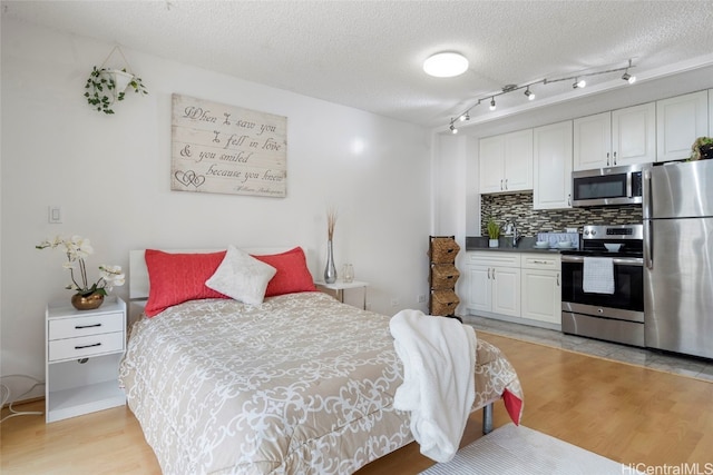 bedroom featuring stainless steel fridge, a textured ceiling, and light hardwood / wood-style flooring