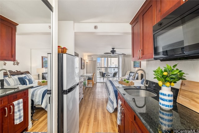 kitchen with ceiling fan, sink, dark stone countertops, stainless steel fridge, and light hardwood / wood-style floors