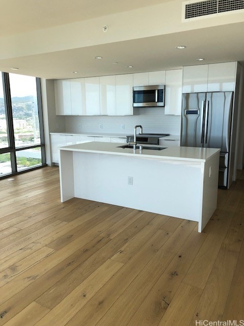 kitchen with light hardwood / wood-style floors, appliances with stainless steel finishes, a center island with sink, and white cabinets