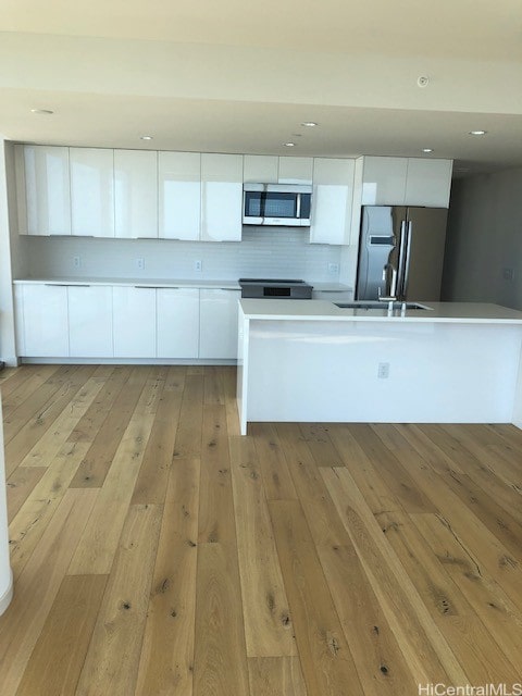 kitchen with light wood-type flooring, a kitchen island, white cabinetry, and stainless steel appliances