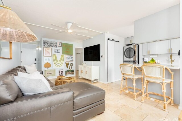 living room with a barn door, ceiling fan, stacked washer / dryer, and light tile patterned floors