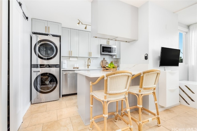 kitchen featuring a breakfast bar, kitchen peninsula, appliances with stainless steel finishes, light tile patterned floors, and stacked washing maching and dryer