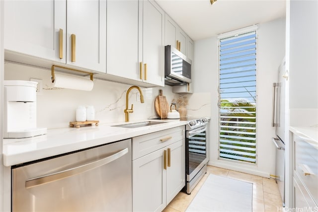 kitchen with stainless steel appliances, light stone countertops, white cabinets, and sink