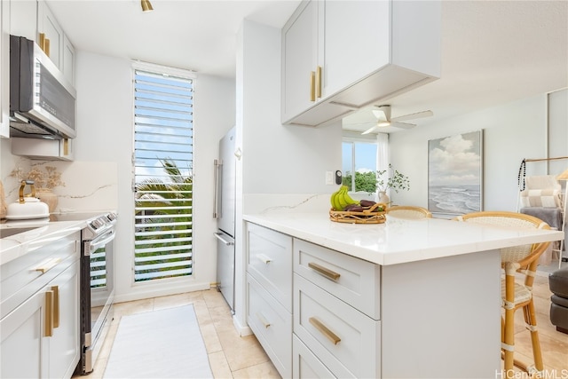 kitchen with backsplash, ceiling fan, appliances with stainless steel finishes, white cabinets, and a breakfast bar area