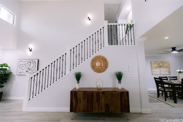 staircase featuring wood-type flooring, ceiling fan, and a towering ceiling