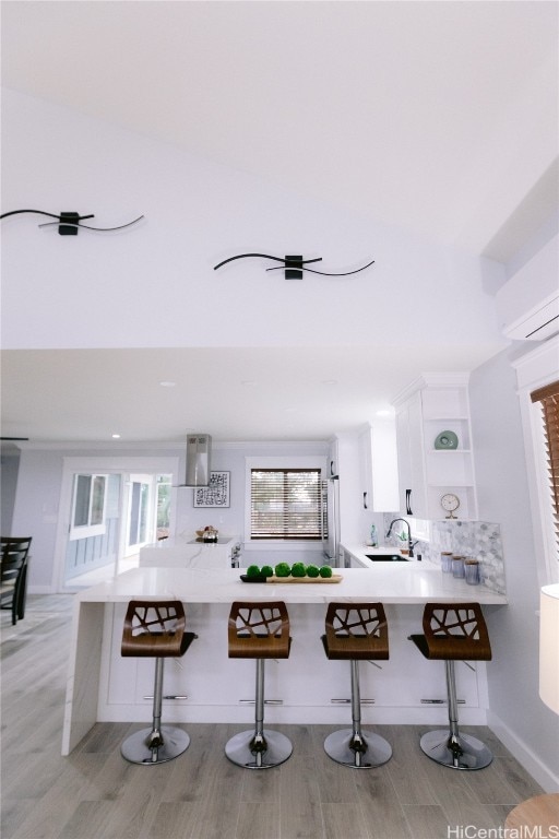 kitchen with sink, kitchen peninsula, a breakfast bar area, light hardwood / wood-style flooring, and white cabinets