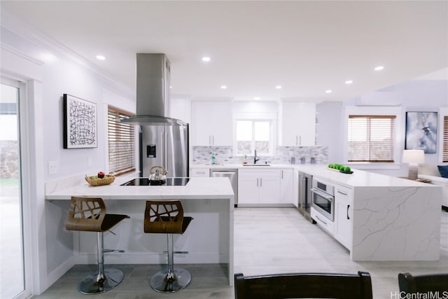 kitchen with island range hood, a breakfast bar area, tasteful backsplash, white cabinetry, and appliances with stainless steel finishes