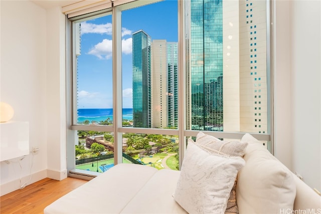 bedroom with hardwood / wood-style flooring, a wall of windows, a water view, and multiple windows