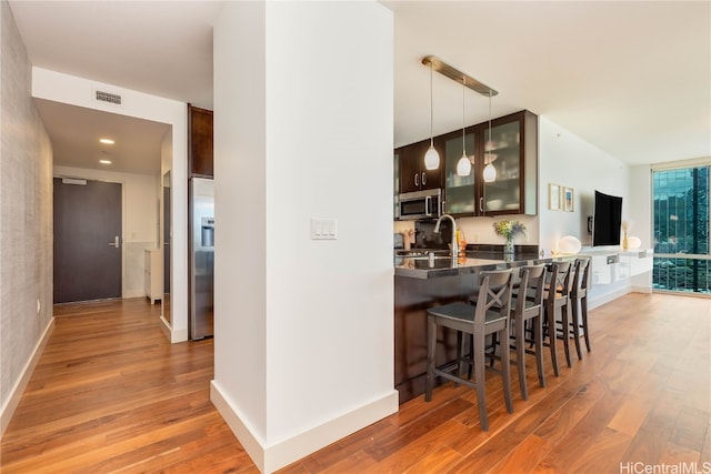 kitchen with kitchen peninsula, a breakfast bar, light wood-type flooring, appliances with stainless steel finishes, and decorative light fixtures