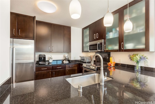 kitchen with stainless steel appliances, dark stone counters, hanging light fixtures, sink, and dark brown cabinets