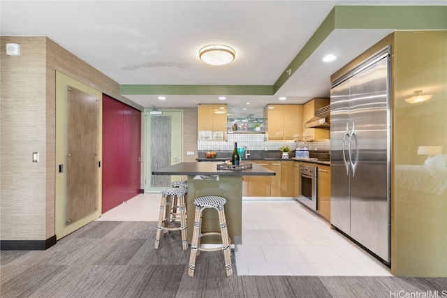 kitchen featuring appliances with stainless steel finishes, a kitchen breakfast bar, light brown cabinetry, wall chimney exhaust hood, and a center island