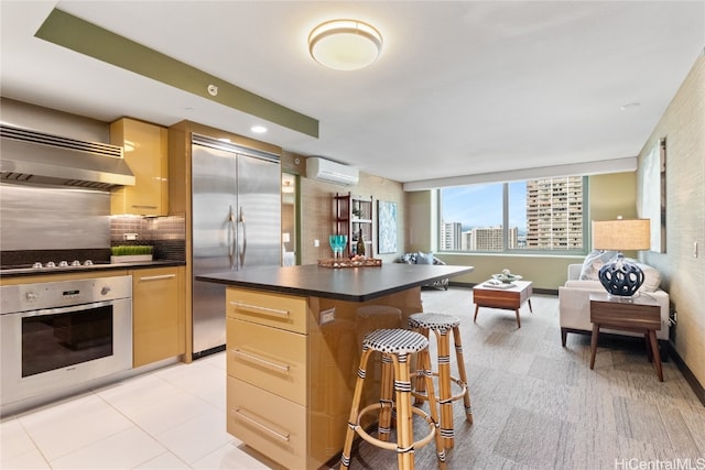 kitchen with a kitchen bar, a center island, wall chimney exhaust hood, appliances with stainless steel finishes, and an AC wall unit