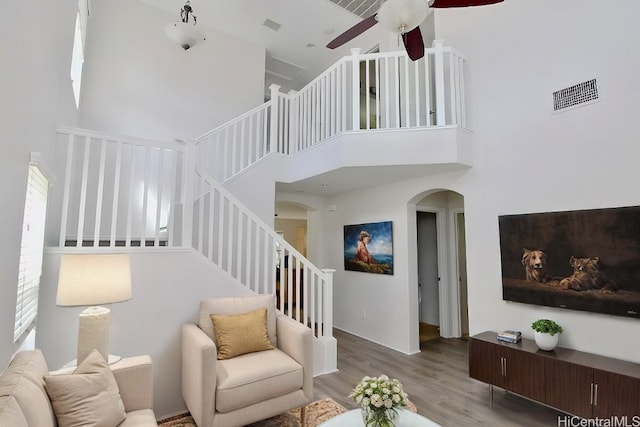 living room featuring a towering ceiling, light hardwood / wood-style flooring, and ceiling fan