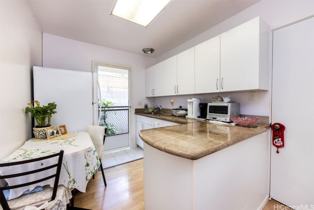 kitchen featuring white refrigerator, sink, kitchen peninsula, light hardwood / wood-style floors, and white cabinetry