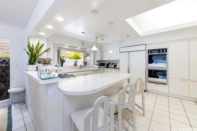 kitchen with kitchen peninsula, a breakfast bar, stainless steel double oven, pendant lighting, and white cabinetry