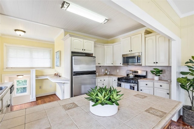 kitchen featuring decorative backsplash, crown molding, tile counters, and appliances with stainless steel finishes