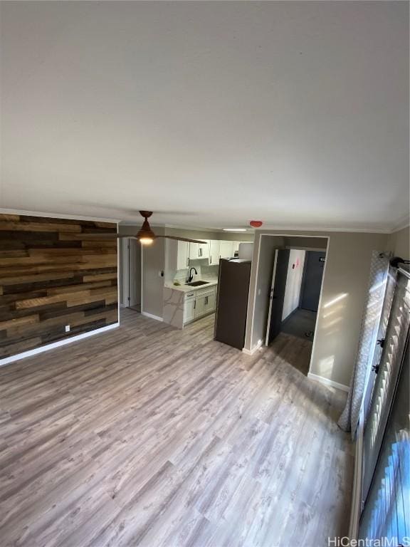 unfurnished living room featuring crown molding, sink, wooden walls, and light hardwood / wood-style floors