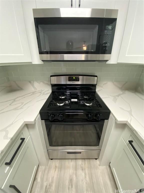 kitchen featuring light stone counters, white cabinetry, stainless steel appliances, and tasteful backsplash