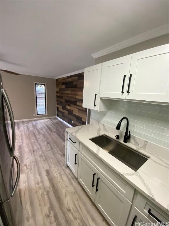 kitchen with refrigerator, sink, wooden walls, white cabinetry, and light stone counters