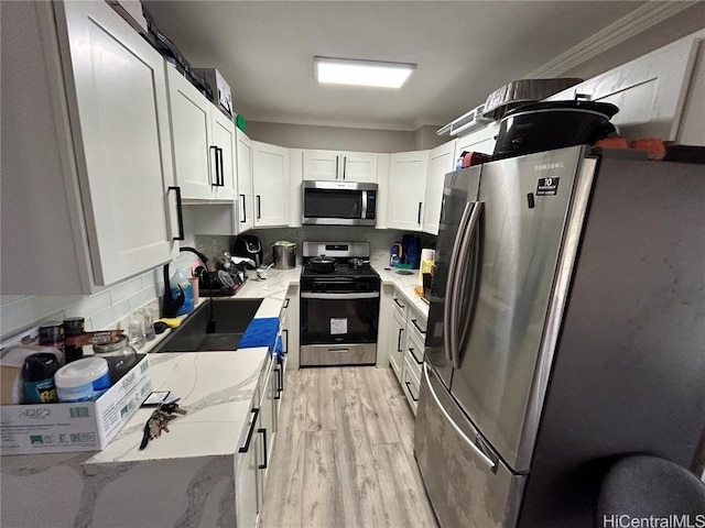 kitchen with white cabinetry, appliances with stainless steel finishes, crown molding, light stone counters, and sink