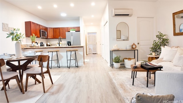 kitchen with light hardwood / wood-style floors, a breakfast bar, kitchen peninsula, appliances with stainless steel finishes, and an AC wall unit