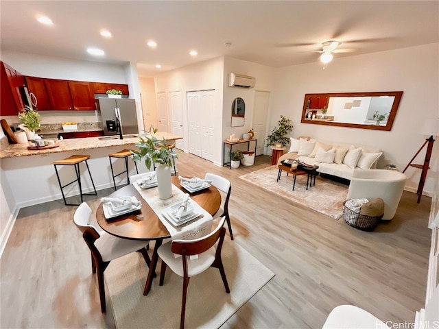 dining area with a wall unit AC, light hardwood / wood-style floors, and ceiling fan