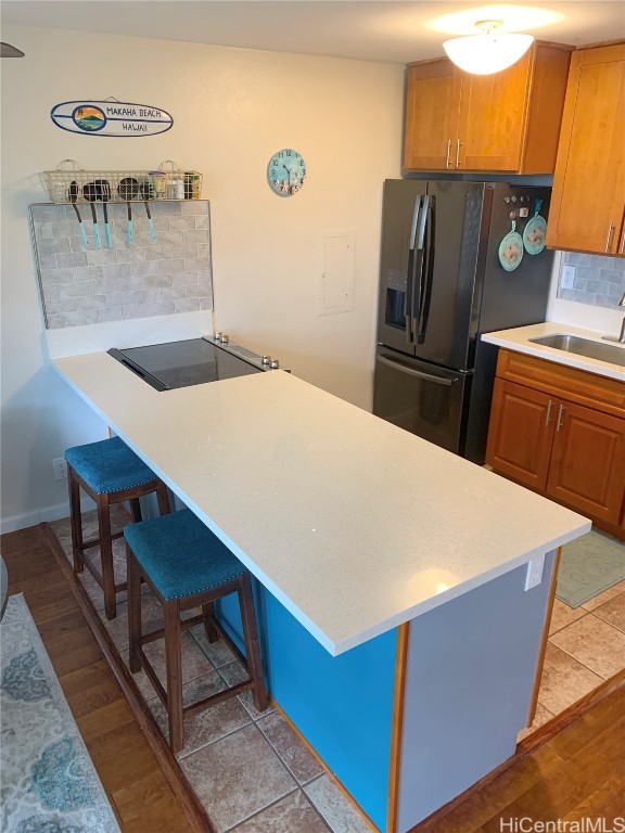 kitchen with sink, light hardwood / wood-style flooring, backsplash, black appliances, and a kitchen bar