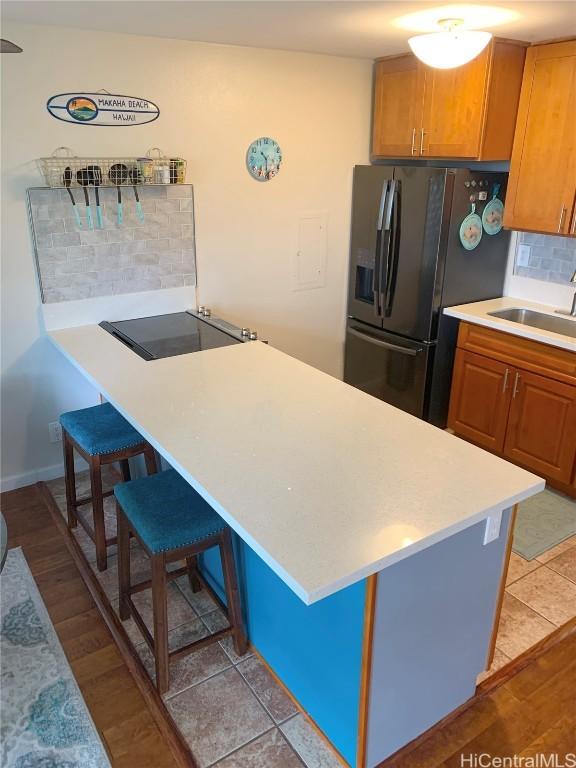 kitchen with light countertops, backsplash, a sink, black appliances, and a kitchen bar