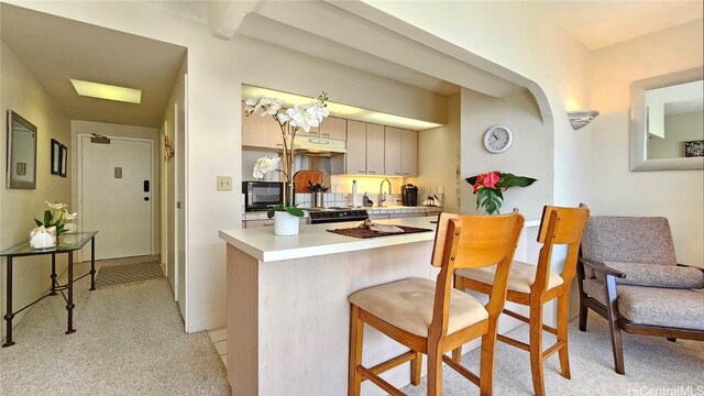 kitchen with a kitchen bar, kitchen peninsula, light carpet, and sink