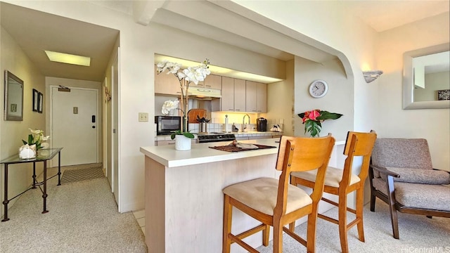 kitchen with light carpet, a sink, a kitchen breakfast bar, black microwave, and light countertops