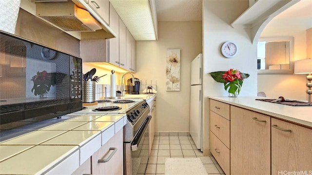 kitchen with under cabinet range hood, tile countertops, light tile patterned floors, electric stove, and arched walkways