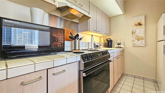 kitchen featuring under cabinet range hood, tile countertops, light tile patterned flooring, electric range, and a sink