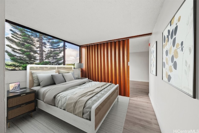 bedroom with a textured ceiling, light hardwood / wood-style flooring, and expansive windows