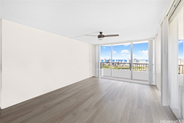 empty room featuring wood-type flooring, a textured ceiling, floor to ceiling windows, and ceiling fan